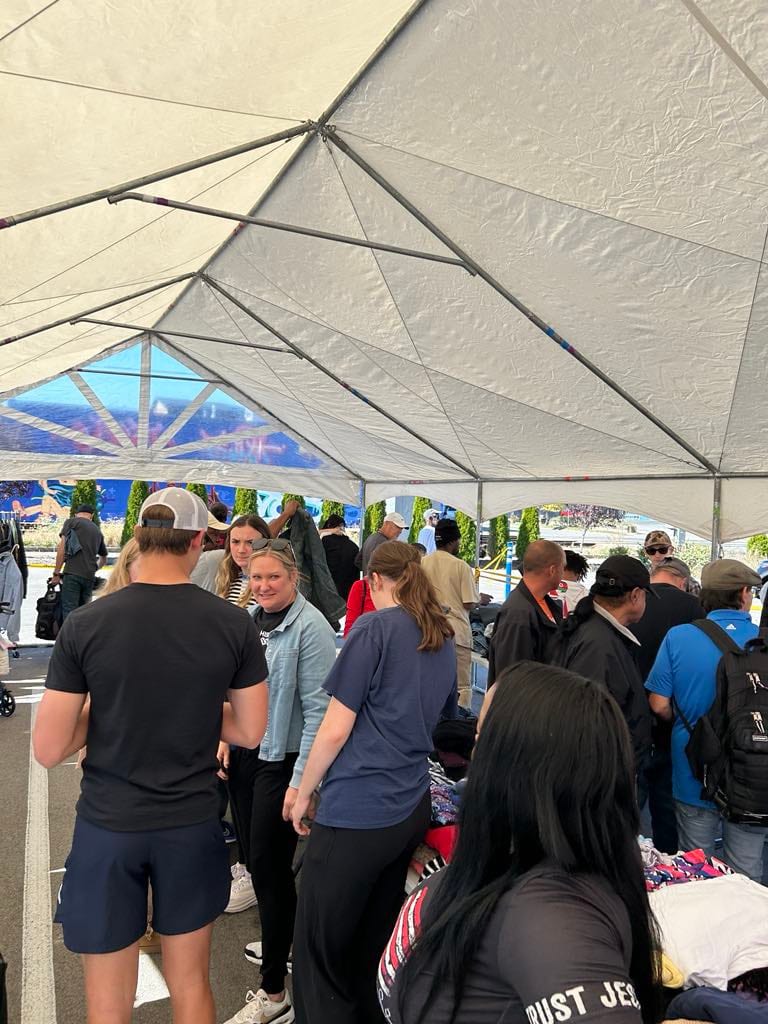 A crowd of guests and volunteers browsing clothing racks together under a large white tent